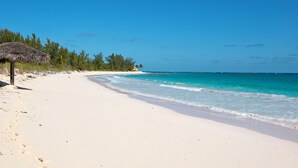 A beach with a thatched umbrella, clear turquoise waters, and a white sandy shore. - Buttonwood Bliss: Lux Condo With Views (James Cistern)