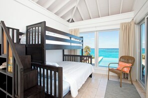 A bedroom with a bunk bed, a chair with a cushion, and a view of the ocean. - Touch Of Class Cottage: Beachfront Oasis (Savannah Sound)