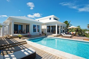 A modern house with a swimming pool, outdoor furniture, and a deck. - Touch Of Class Cottage: Beachfront Oasis (Savannah Sound)