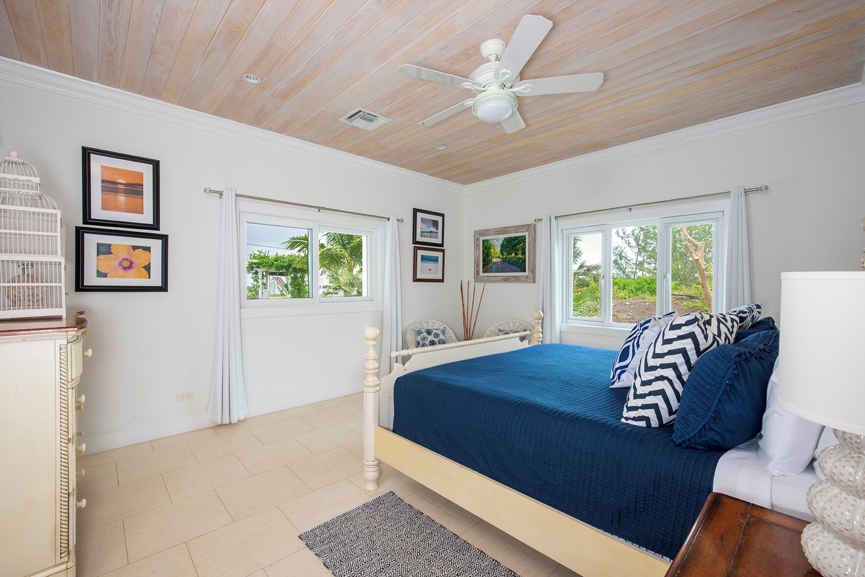 A bedroom with a bed, two windows, a ceiling fan, and a view of greenery outside.