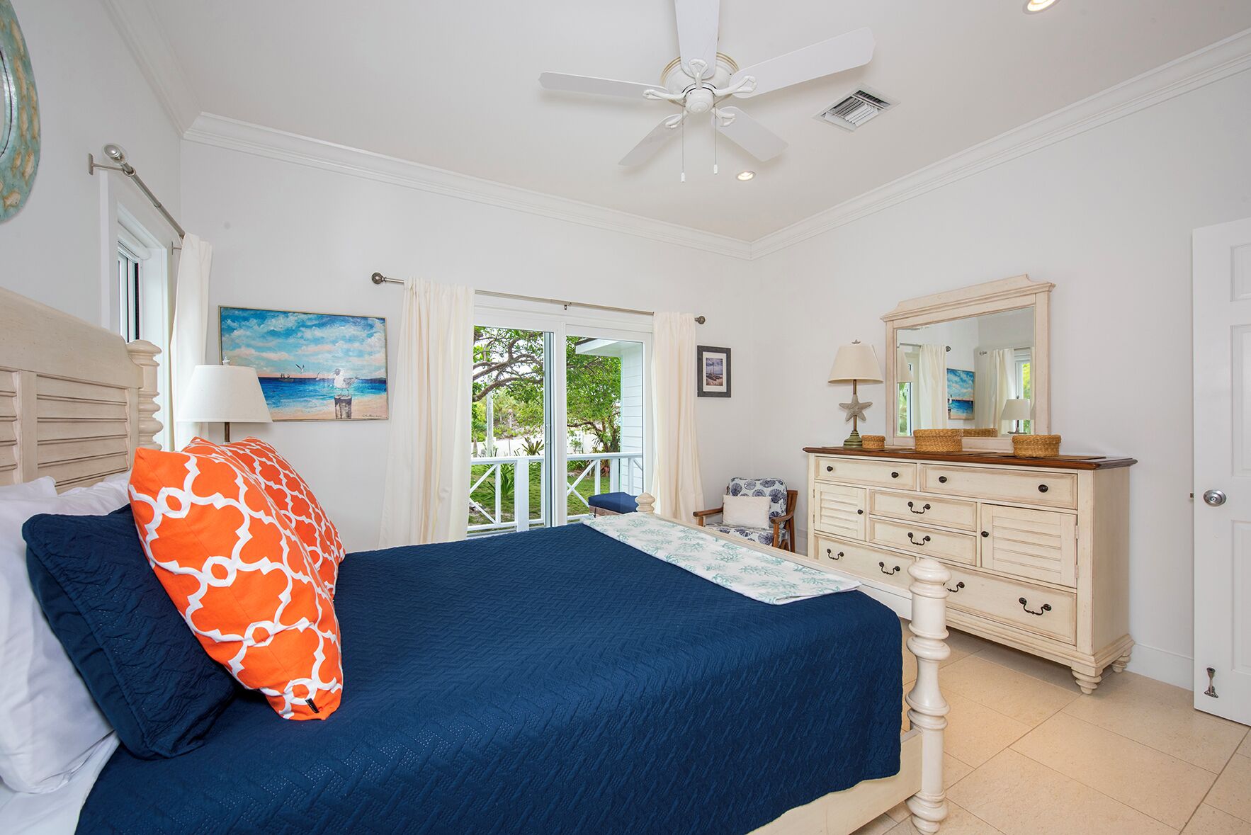 A bedroom with a bed, a dresser, a ceiling fan, and a view of the outdoors.