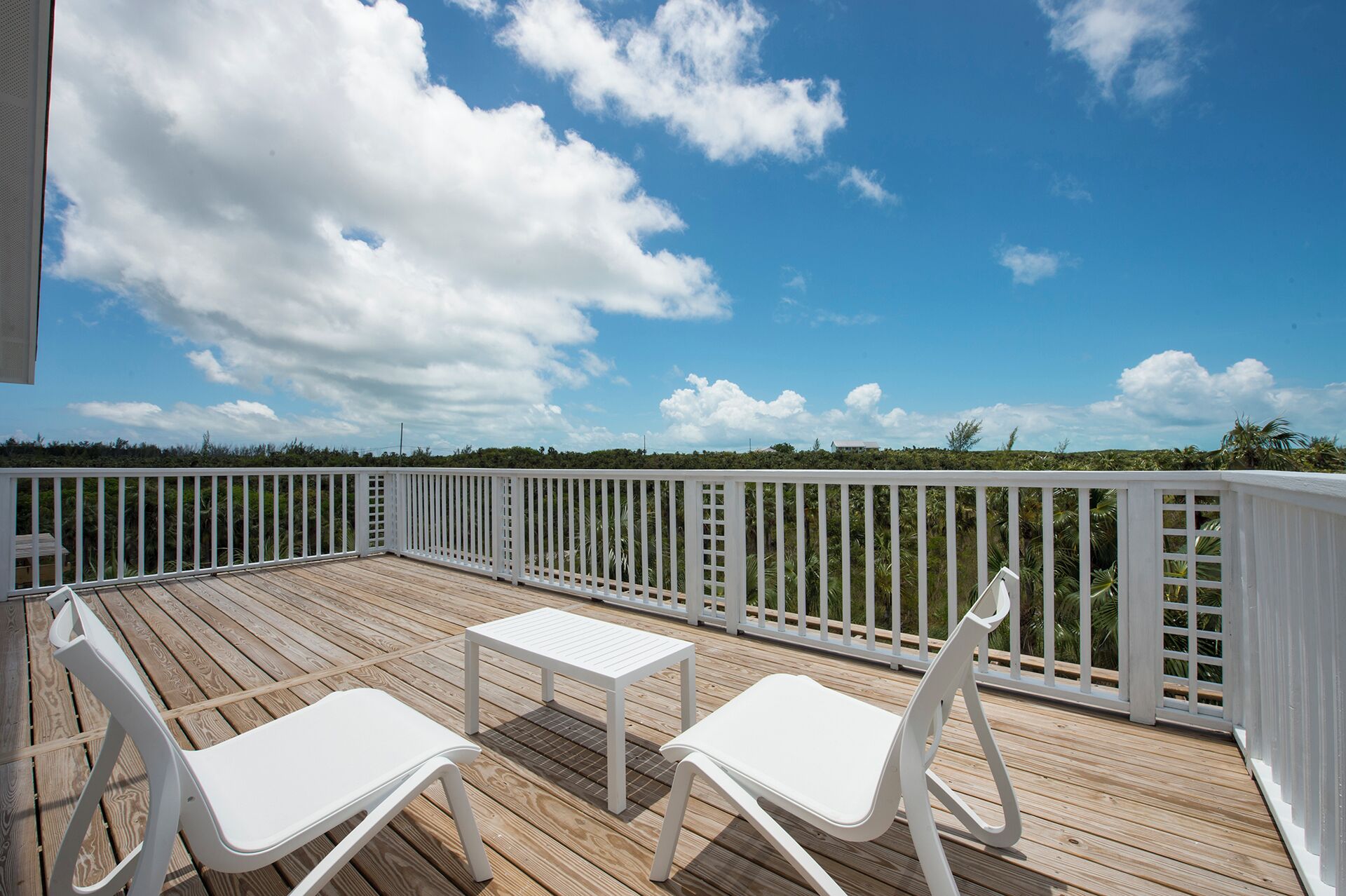 A wooden deck with white railings, two white chairs, and a small table.