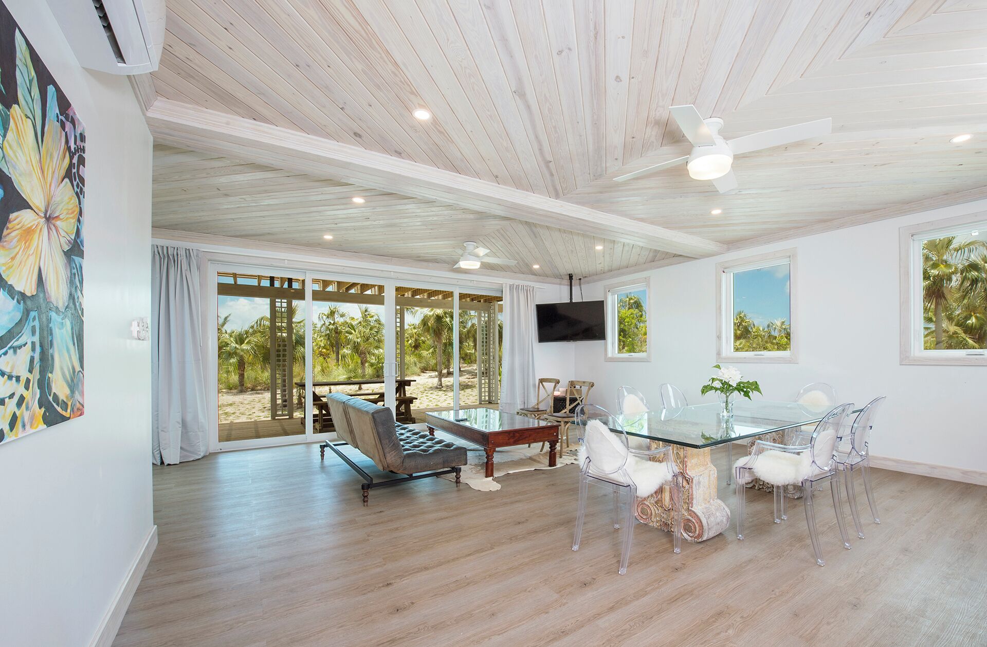 A spacious room with a glass dining table, clear chairs, a sofa, and a ceiling fan.
