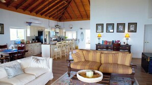 Un vaste espace de vie doté d’un plafond haut, une cuisine à l’arrière-plan et un coin repas avec des chaises et une table.