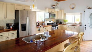 Une cuisine dotée de meubles en bois, d’appareils électroménagers en acier inoxydable, d’un grand îlot central avec un évier et de luminaires suspendus.