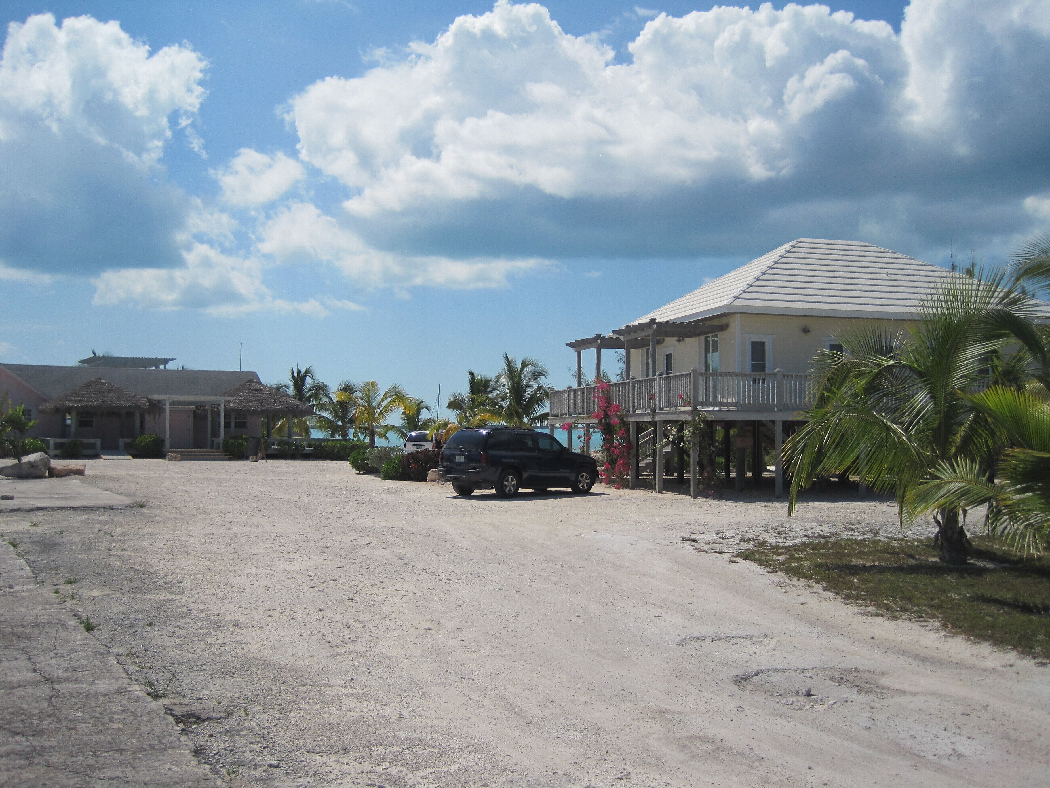 A coastal property with a sandy driveway, a black SUV, and a two-story building with a balcony.