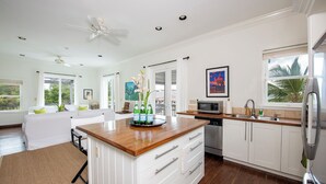 A modern kitchen with white cabinetry, a wooden countertop, and a built-in dishwasher. - Seaside Escape: Private Beachfront Villa With Infinity Pool (Rock Sound)