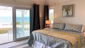 Camera da letto con un letto, una finestra con tende, una lampada e vista sulla spiaggia.