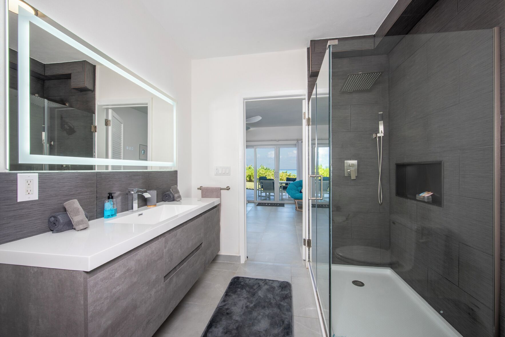Un baño moderno con un espejo grande, lavamanos dobles y cabina de ducha con mampara de vidrio.