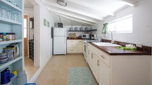 A compact kitchen with a refrigerator, microwave, stove, and sink. There are shelves with jars and a fan above the refrigerator. - Harbour Island Haven: Newly Remodeled Cottage Near Pink Sands Beach (Dunmore Town)