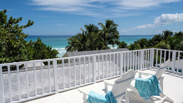 A balcony with white railings overlooking a beach with palm trees and the ocean. - Harbour Island Haven: Newly Remodeled Cottage Near Pink Sands Beach (Dunmore Town)