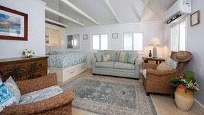 A spacious living room with a large bed, a sofa, and a chair, a ceiling fan, and an air conditioning unit. - Harbour Island Haven: Newly Remodeled Cottage Near Pink Sands Beach (Dunmore Town)