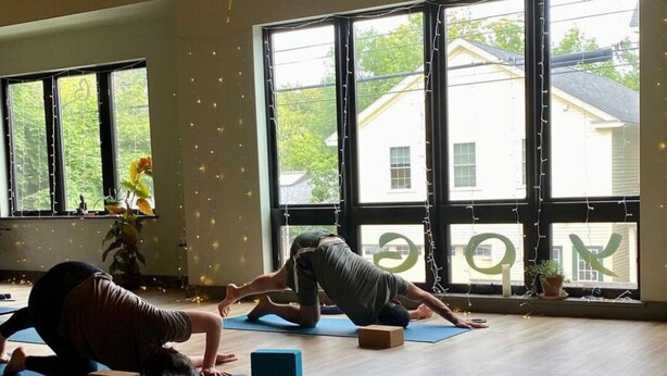 Un estudio de yoga con amplios ventanales, suelos de madera y colchonetas de yoga.