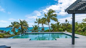 A wooden deck with a pool, palm trees, and a view of the ocean. - Island Escape: Secluded Beachfront Cottage With Pool (North Palmetto Point)
