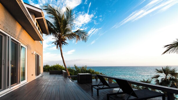 A wooden deck with a lounge chair and a small table, overlooking the ocean. - Island Escape: Secluded Beachfront Cottage With Pool (North Palmetto Point)
