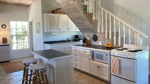 Une cuisine avec un escalier en bois, des meubles blancs, une cuisinière et un coin bar avec des tabourets.