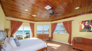 A bedroom with a bed, a dresser, a nightstand, a window with a view of the beach, and a painting on the wall. - Banks Road Bliss: Luxury Estate With Pool (South Palmetto Point)