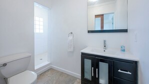 A bathroom with a toilet, a sink with a mirror, and a shower. - Banks Road Bliss: Luxury Estate With Pool (South Palmetto Point)