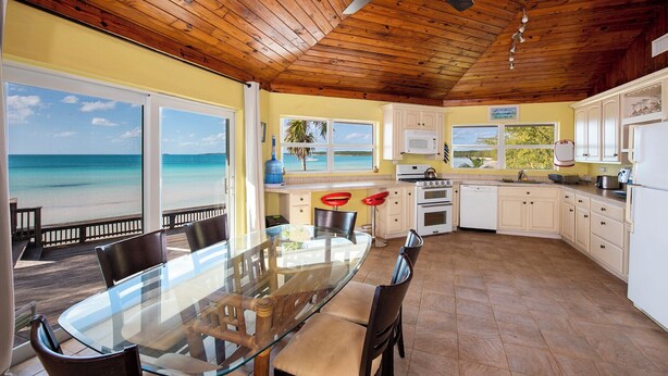 A kitchen with a view of the beach, wooden ceiling, and a dining area with a glass table. - Banks Road Bliss: Luxury Estate With Pool (South Palmetto Point)