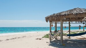 Uma cabana de praia com telhado de palha, uma rede e vista para o oceano.