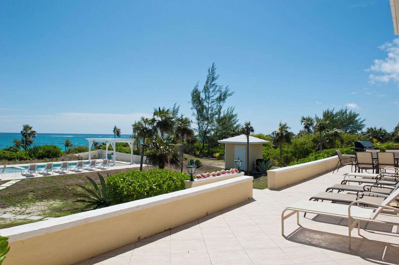 A resort pool area with lounge chairs, a small gazebo, and a view of the ocean.