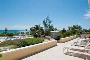 Área de piscina de un resort con sillones reclinables, un pequeño pabellón y vistas al océano.