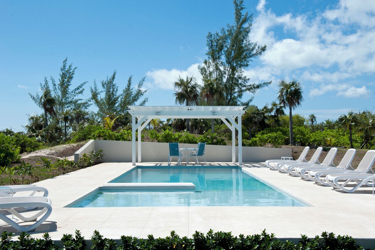 Zona de piscina con pérgola, sillones de descanso y vista al océano.