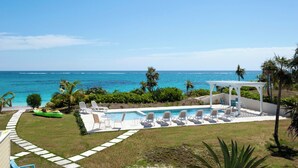 Área de piscina com espreguiçadeiras e um bangalô com vista para o oceano.