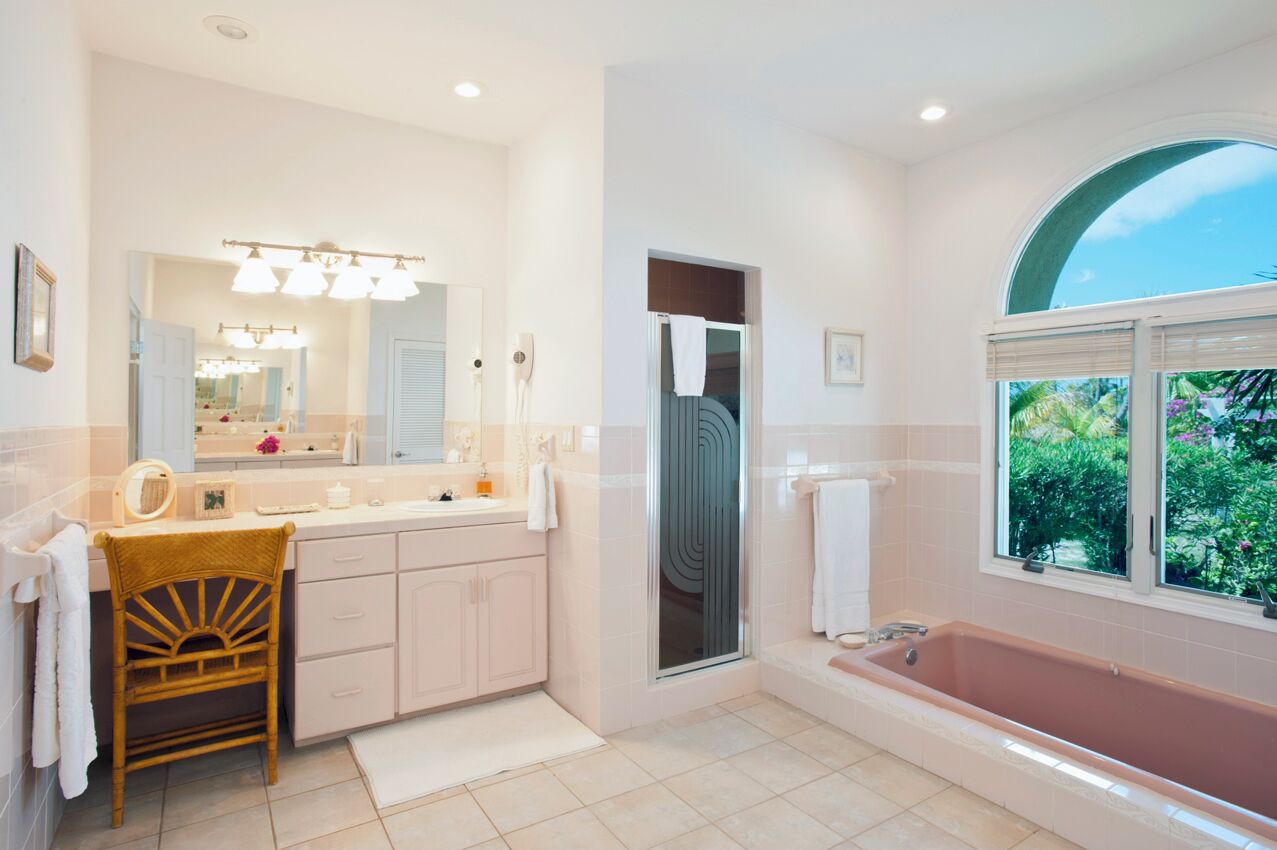 A spacious bathroom with a large vanity, a freestanding bathtub, and a window providing a view of greenery.
