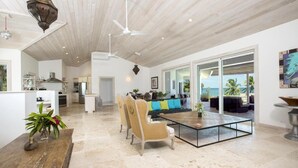 Een ruime woonkamer met houten plafond, een eettafel met stoelen en een groot raam met uitzicht op de oceaan.