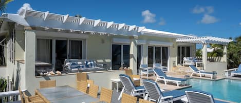 A poolside area with lounge chairs, a dining table, and a covered patio.