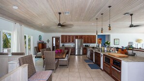 Una cocina amplia con armarios de madera, un refrigerador de acero inoxidable y un comedor con mobiliario de mimbre.