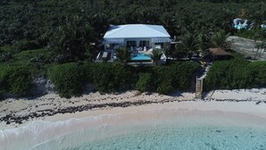 Vista aérea de una propiedad frente a la playa con una casa grande, una piscina y exuberante vegetación.