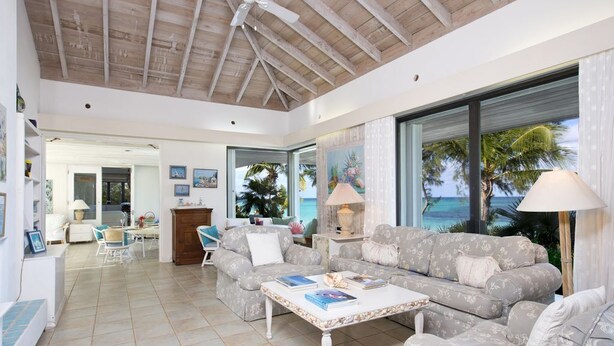 A spacious living room with a ceiling fan, a large window with a view of the ocean, a sofa set, and a coffee table. - Tropical Hideaway: Charming Cottage Near Pink Sands Beach (Rock Sound)