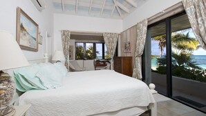 A bedroom with a bed, a desk, and a view of the ocean through large windows. - Tropical Hideaway: Charming Cottage Near Pink Sands Beach (Rock Sound)