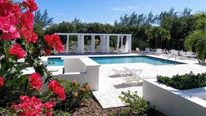 Un área de piscina con sillas reclinables blancas y una pérgola.