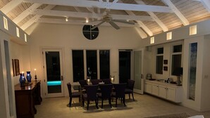 Un vaste espace de vie comprenant une table à manger, des chaises et un ventilateur de plafond. Une porte-fenêtre coulissante donne accès à la zone de la piscine.