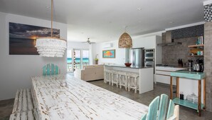 A modern kitchen with a central island, bar stools, and a view of the ocean. - Secluded Luxury: New Beachfront Home With Pool (Gregory Town)