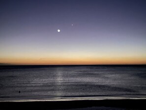 A beach at dusk with a calm sea and a visible moon in the sky. - Secluded Luxury: New Beachfront Home With Pool (Gregory Town)