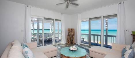 Een ruim balkon met uitzicht op de oceaan, voorzien van twee banken en een ronde houten salontafel.