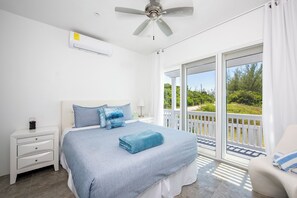 A bedroom with a bed, a nightstand, a ceiling fan, and a view of the outdoors through a sliding glass door. - Secluded Luxury: New Beachfront Home With Pool (Gregory Town)