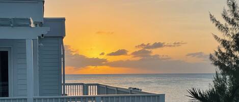 Un edificio frente al mar con balcón, durante la puesta de sol.
