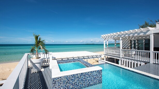 A pool area with clear blue water, a white deck, and a view of the ocean. - Secluded Luxury: New Beachfront Home With Pool (Gregory Town)