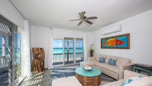 A spacious living room with a large sliding glass door leading to a balcony with a view of the ocean. - Secluded Luxury: New Beachfront Home With Pool (Gregory Town)