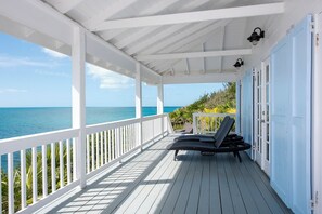 Ein überdachter Außenbereich mit Holzdeck, weißen Geländern und Blick aufs Meer.
