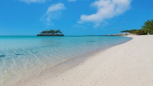 Ein Strand mit klarem türkisblauem Wasser, einem sandigen Ufer und einer kleinen Insel mit Bäumen in der Ferne.