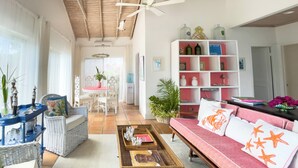 Amplia sala de estar con techo alto, ventilador de techo, comedor con mesa rosa y sofá rosa con almohadas estampadas de estrellas.