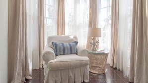 A room with a white armchair, a glass side table with a lamp, and sheer curtains. - Captain'S Quarters: Restored Waterfront Home With Sunset Views (Governor's Harbour)
