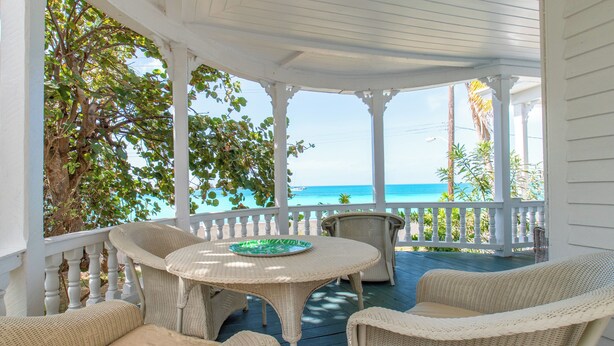 A covered porch with wicker furniture and a view of the ocean. - Captain'S Quarters: Restored Waterfront Home With Sunset Views (Governor's Harbour)