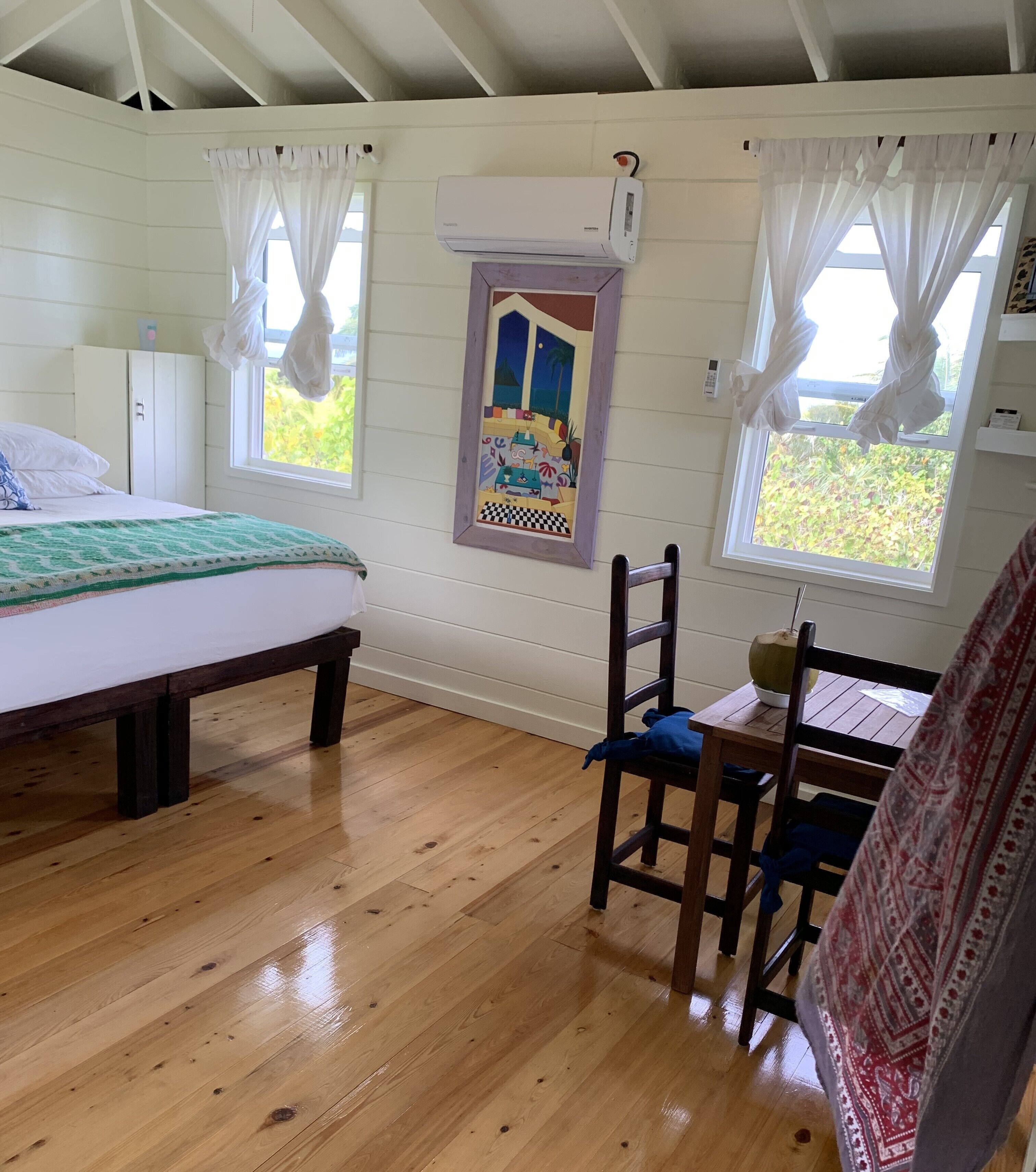 Una habitació amb un llit, una taula i cadires, una finestra amb cortines i un aparell d'aire condicionat.